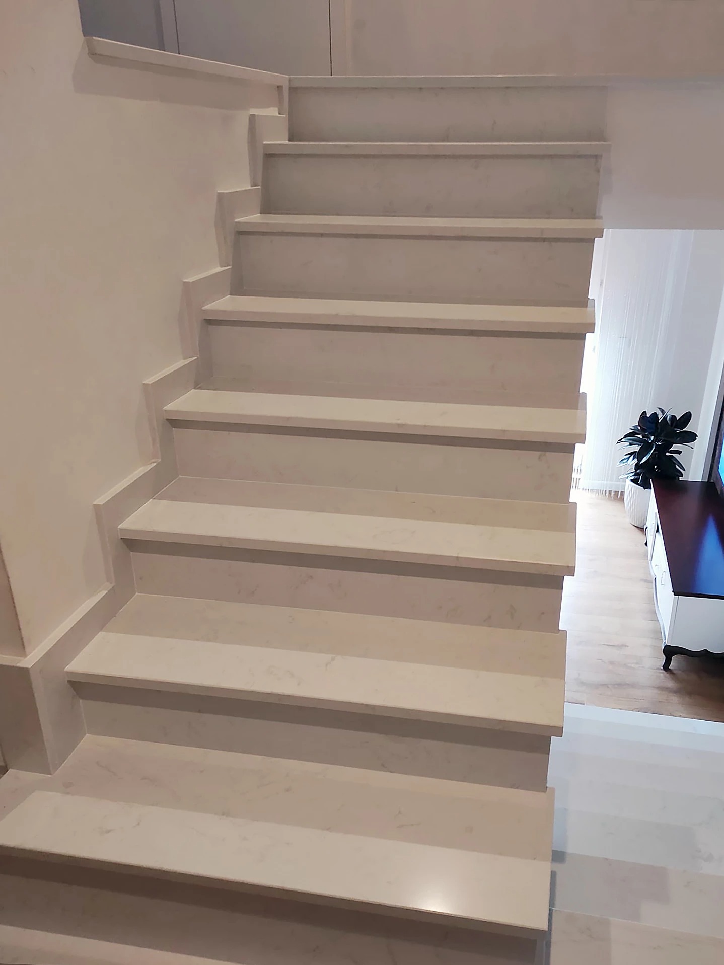 Jasne, marmurowe schody wewnętrzne z subtelnym wzorem, widoczne z dołu, z fragmentem salonu w tle, ukazujące precyzjne wykończenie i minimalistyczny design.