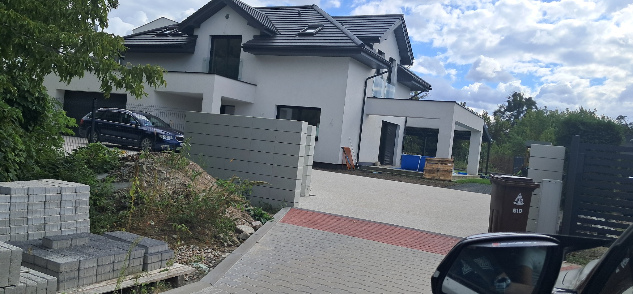 Nowoczesny dom jednorodzinny z garażem, widok z zewnątrz. Na pierwszym planie kostka brukowa i materiały budowlane.