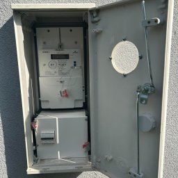 ACE SYSTEM Adrian Finowski - Otwarta skrzynka z licznikiem energii elektrycznej i zabezpieczeniami na zewnątrz budynku w Jeleniej Górze. Widoczne elementy instalacji elektrycznej.