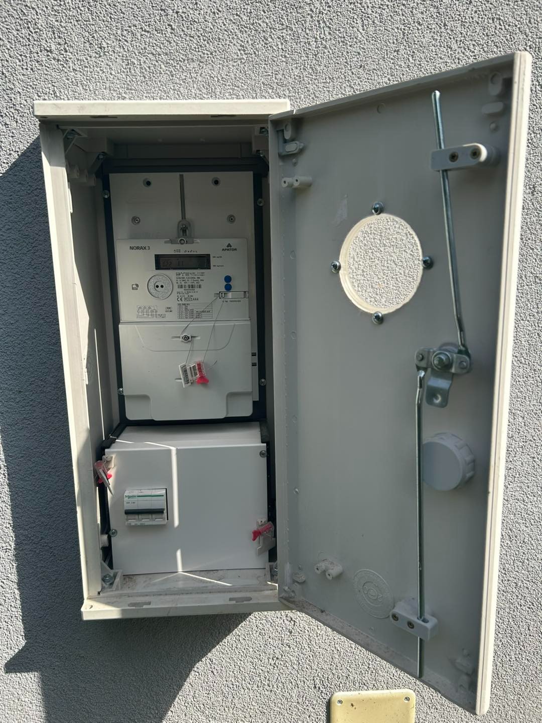 Otwarta skrzynka z licznikiem energii elektrycznej i zabezpieczeniami na zewnątrz budynku w Jeleniej Górze. Widoczne elementy instalacji elektrycznej.