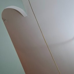 Sobut - Ściana po szpachlowaniu z łukowatym przejściem, świeżo pomalowana na dwa kolory. Widoczne narzędzia malarskie na podłodze i kabel zwisający z sufitu.