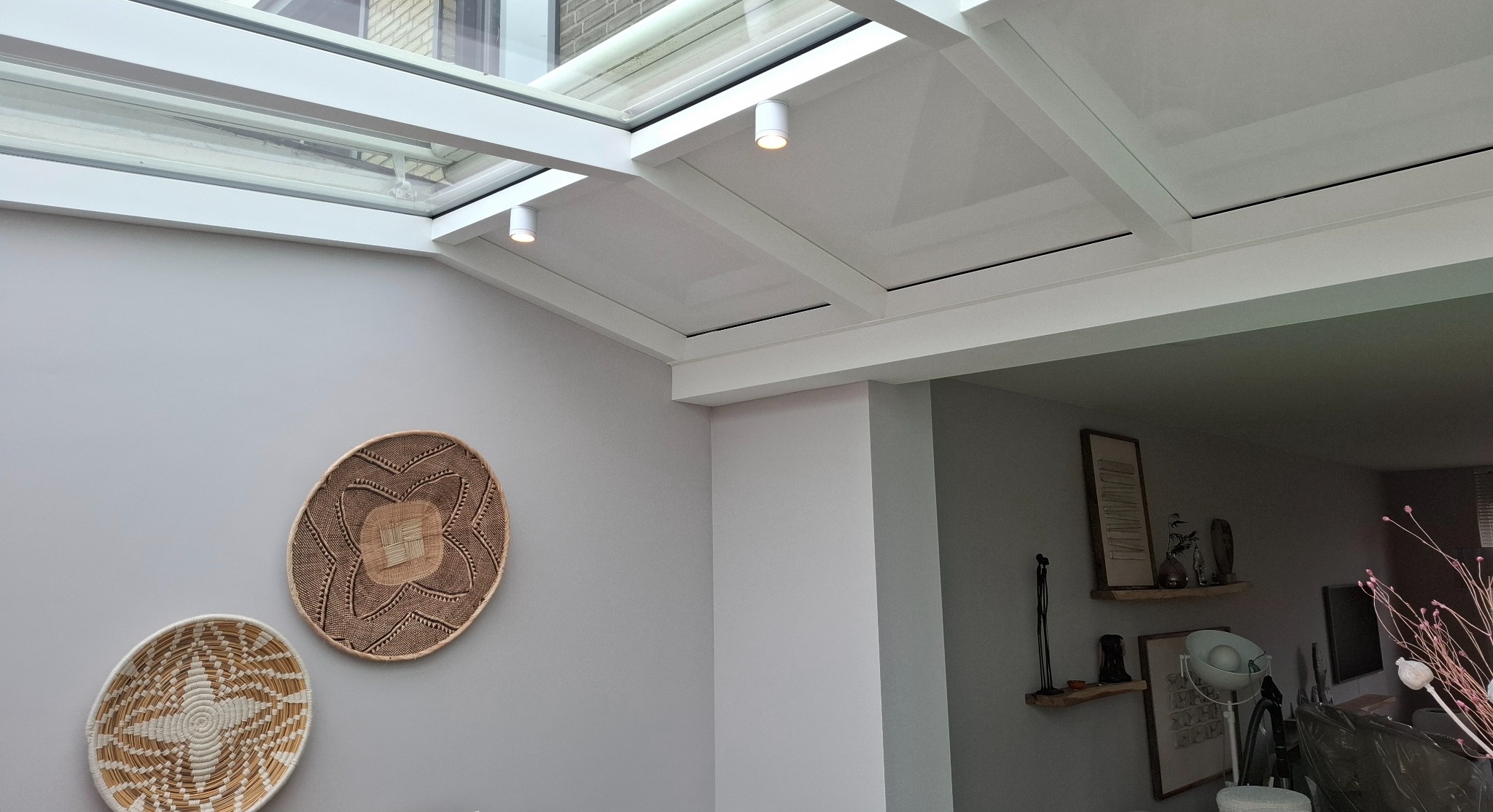 Jasnoszara ściana z dekoracyjnymi koszykami, biały sufit z oknem dachowym i oświetleniem punktowym. Minimalistyczny, nowoczesny design wnętrza.