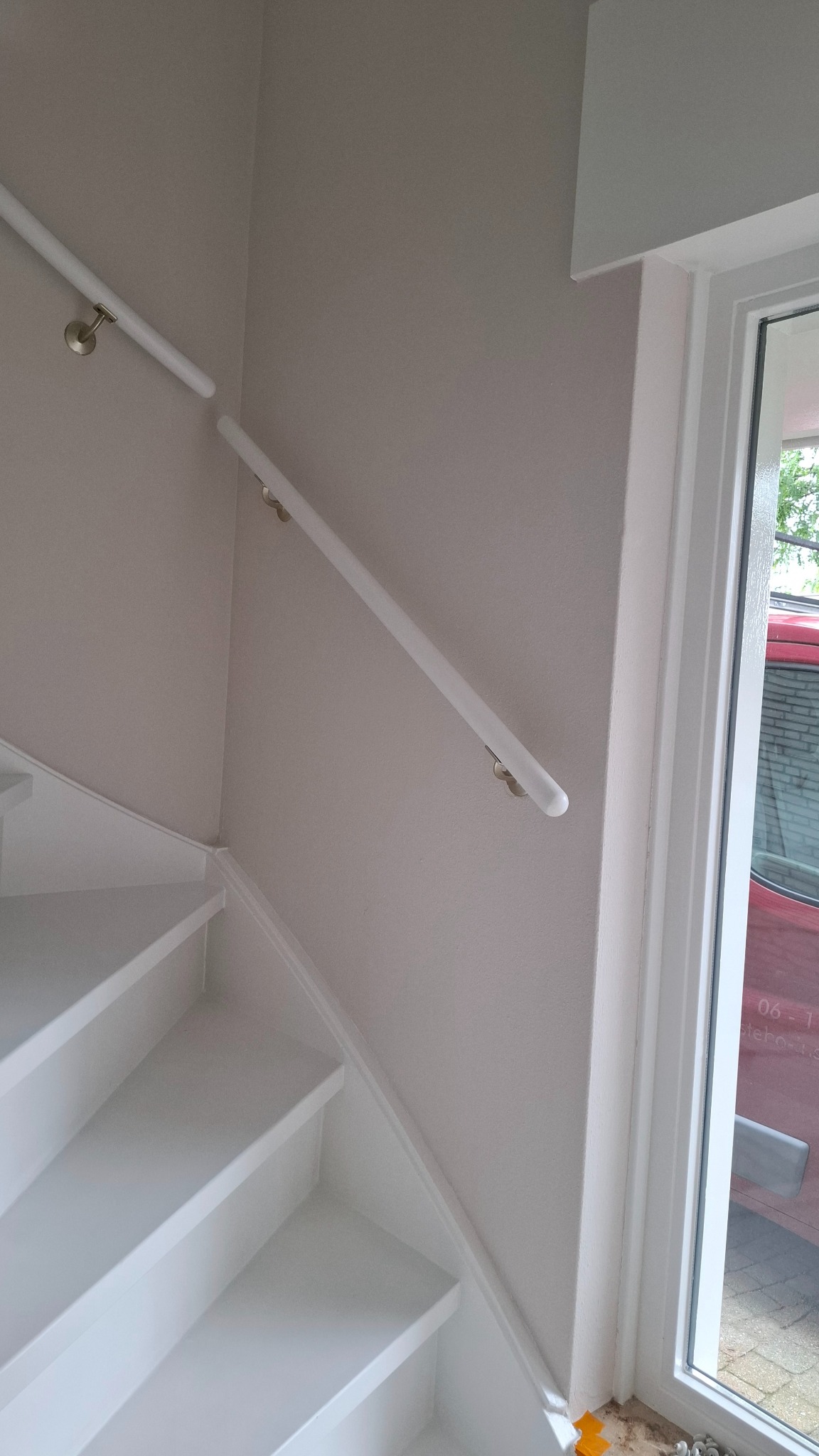 Białe schody z pomalowaną ścianą w odcieniach szarości, z zamontowaną białą poręczą i oknem z widokiem na zewnątrz. Widoczne świeże wykończenie.