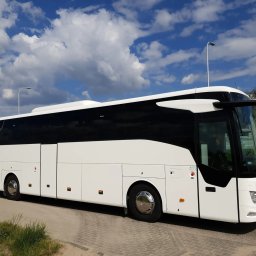 zarezerwujautokar.pl - Nowoczesny autokar turystyczny Mercedes w kolorze białym, zaparkowany na tle błękitnego nieba z chmurami. Widok z boku, oświetlenie dzienne.