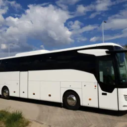 Nowoczesny autokar turystyczny Mercedes w kolorze białym, zaparkowany na tle błękitnego nieba z chmurami. Widok z boku, oświetlenie dzienne.