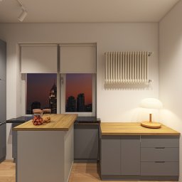 Renata Urban Projekty na 4 kąty - Szara kuchnia z drewnianymi blatami i widokiem na miasto o zmierzchu. Czerwony toster SMEG z pieczywem na blacie. Ciepłe światło lampki stołowej.
