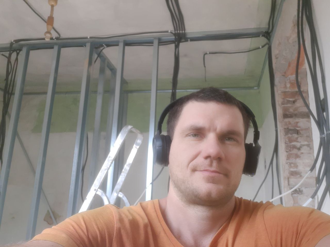 Konstrukcja ścian działowych z profili stalowych, instalacja elektryczna w peszlach na suficie, fragment ściany z cegły. Mężczyzna w słuchawkach na pierwszym planie.