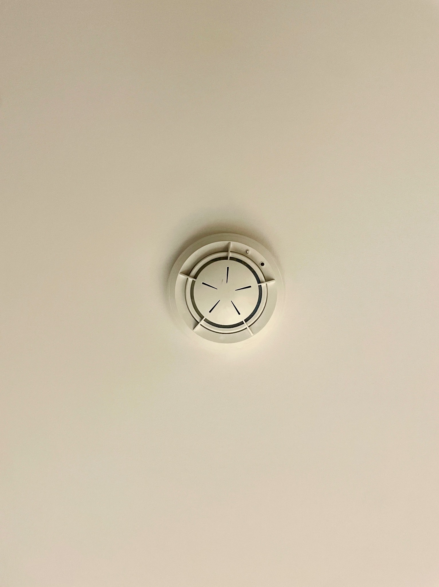 Zamontowany, okrągły czujnik dymu na białym suficie, widziany z dołu. Centralne ujęcie, równomierne oświetlenie. Widoczne detale czujnika.