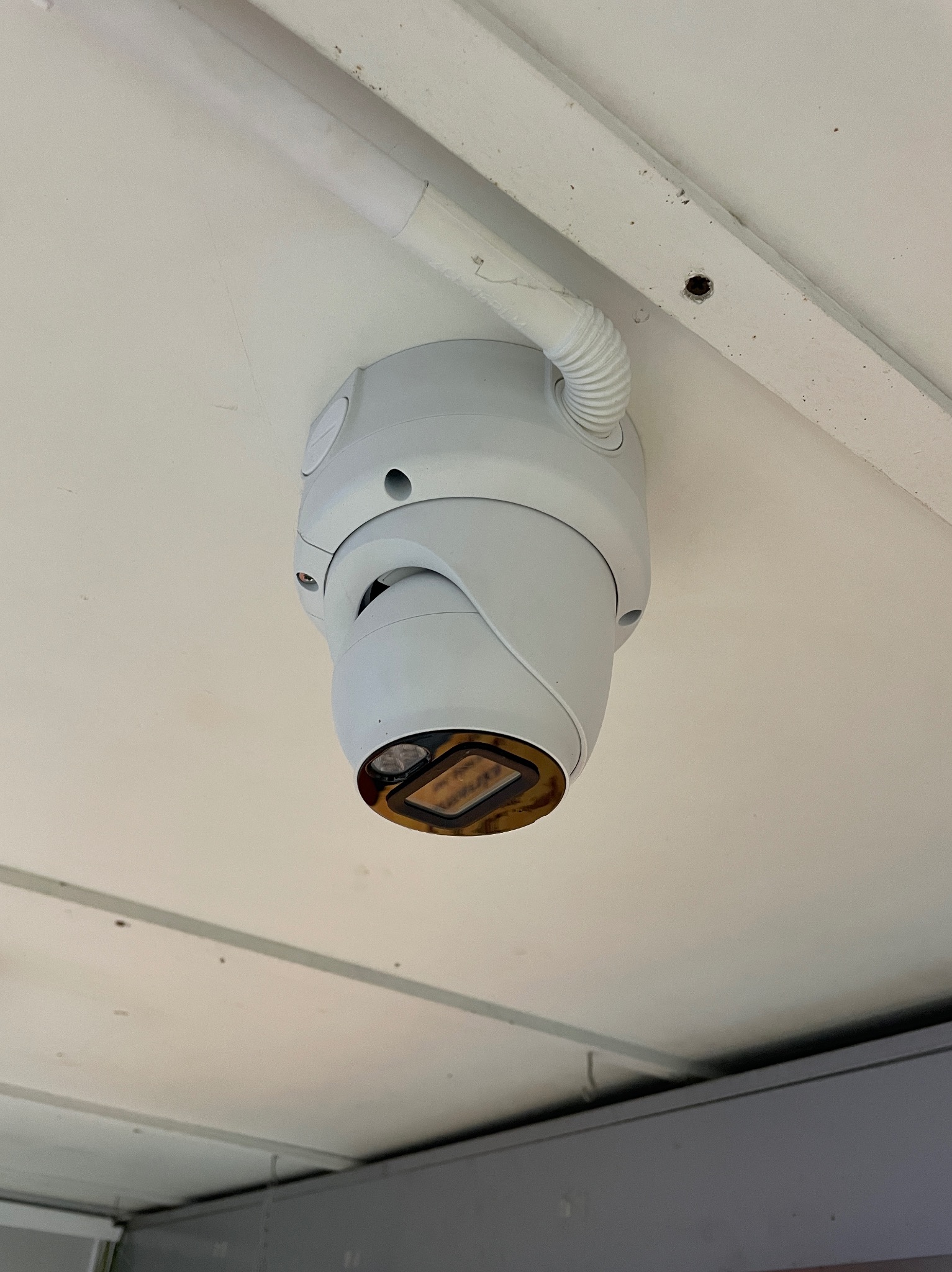 Kamera monitoringu kopułkowa, zamontowana na białym suficie z widoczną rurką kablową. Widok z dołu, na obudowie widoczne ślady użytkowania.