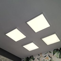 Design & Programming Chyliński Mariusz - Cztery kwadratowe panele LED w suficie, oświetlające pomieszczenie z tapetą w motywy roślinne. Ujęcie z dołu, widoczne fragmenty ściany i sufitu.