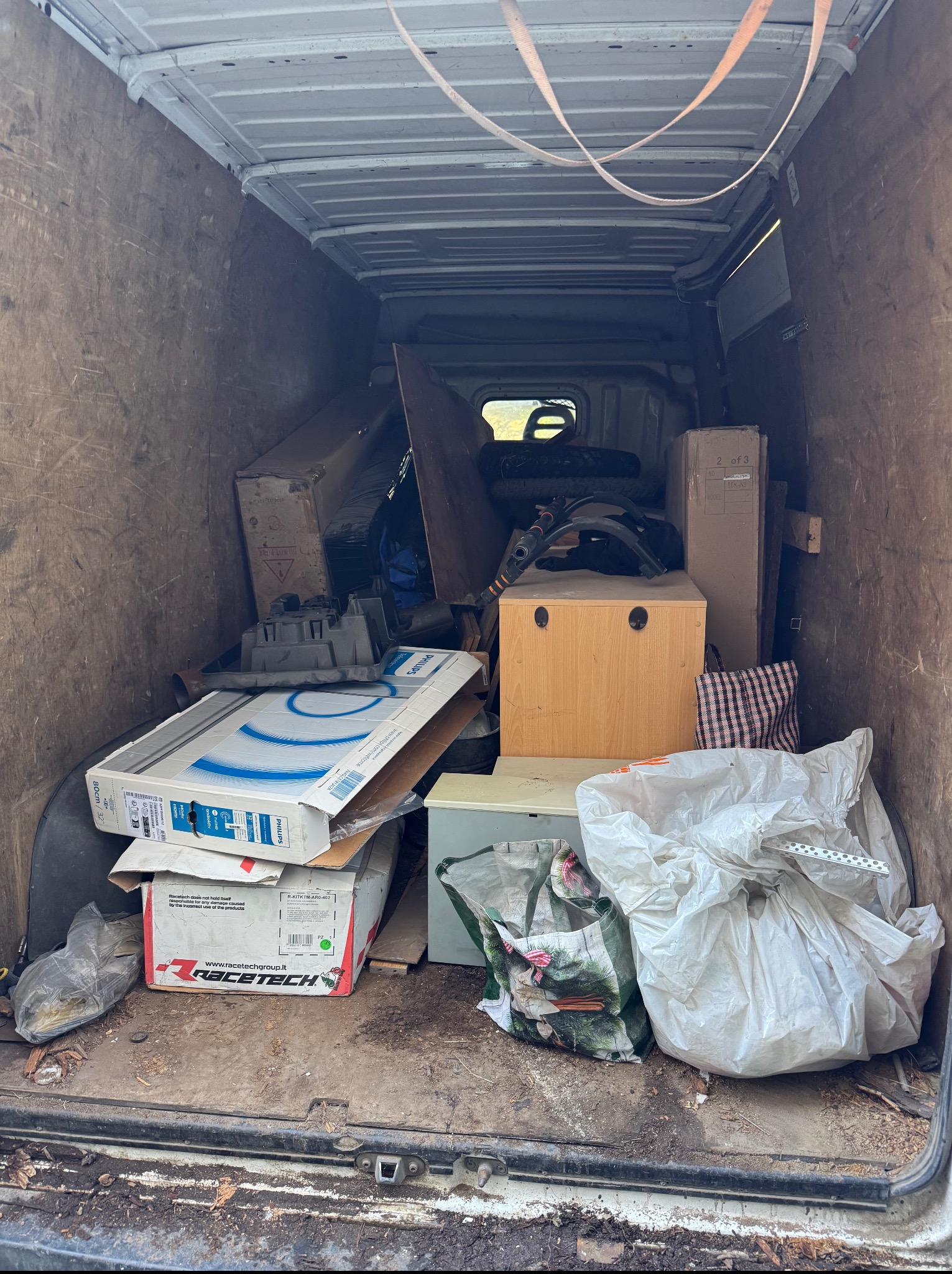 Wnętrze furgonetki wypełnionej różnorodnymi przedmiotami, w tym pudełkami, meblami i torbami, wskazujące na realizację usługi opróżniania mieszkania.