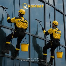 KOMBAT OUTSOURCING SPÓŁKA Z OGRANICZONĄ ODPOWIEDZIALNOŚCIĄ - Dwóch alpinistów w żółto-czarnych strojach myje okna wieżowca za pomocą ściągaczek i wiader. Widoczne logo firmy na ubraniach i budynku.