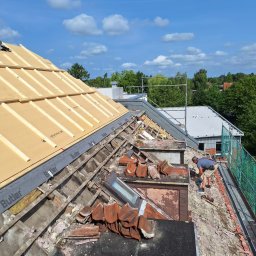 Trockenbau Team - Demontaż starego pokrycia dachowego z widocznymi elementami konstrukcji i oknem dachowym. Prace dekarskie w toku, z fragmentami nowego ocieplenia. Fachowiec przy pracy.