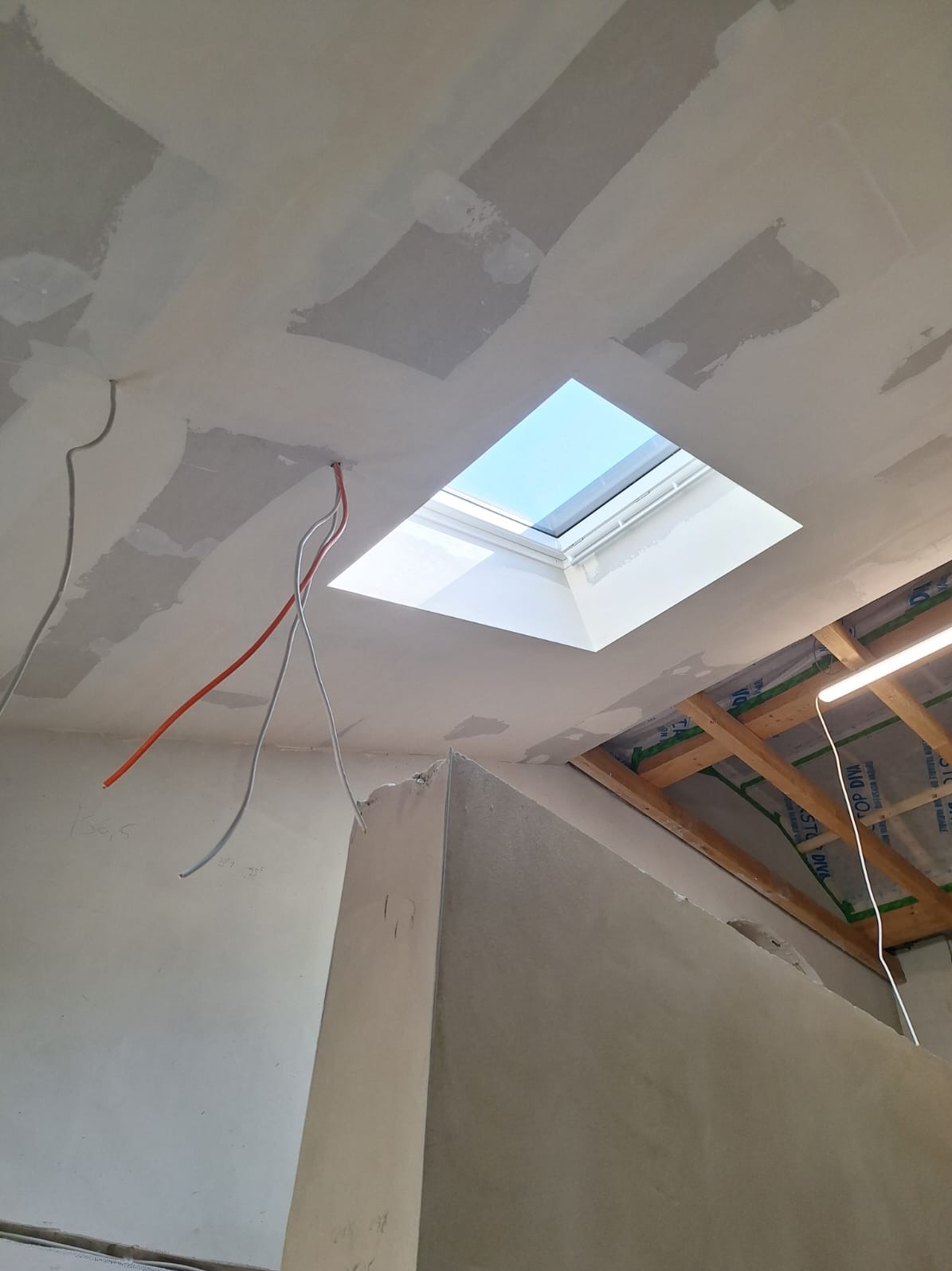 Sufit po szpachlowaniu w Szczecinie, widoczne kable i okno dachowe. Prace wykończeniowe w trakcie realizacji, sufit przygotowany do dalszych prac.