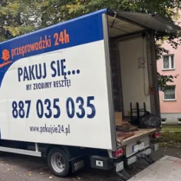 Niebiesko-biała furgonetka z otwartą przestrzenią ładunkową i napisem 'przeprowadzki 24h' na tle bloku mieszkalnego i drzew.