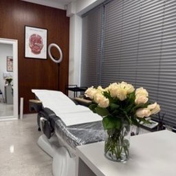 Face Lab Clinic Anna Andrzejewska - Jasny gabinet w Koninie z kozetką, lampą pierścieniową i wazonem białych róż. Na ścianie plakat anatomiczny. Nowoczesne wnętrze salonu.