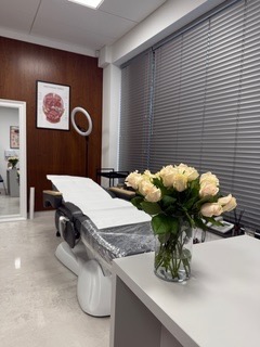 Jasny gabinet w Koninie z kozetką, lampą pierścieniową i wazonem białych róż. Na ścianie plakat anatomiczny. Nowoczesne wnętrze salonu.