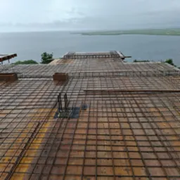 Zbrojenie płyty fundamentowej na deskowaniu z widokiem na jezioro w tle. Konstrukcja z siatki stalowej, przygotowana do zalania betonem. Prace budowlane w toku.