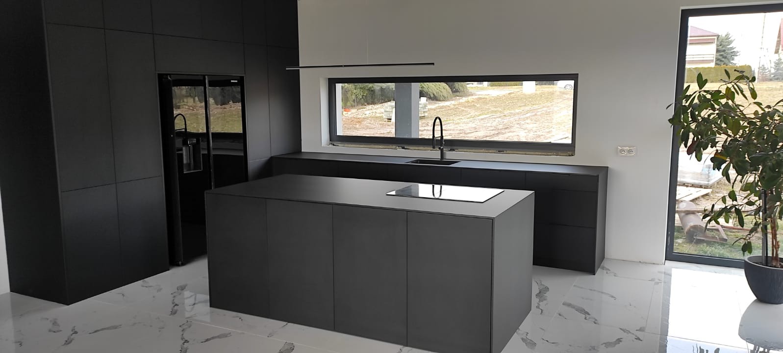 Nowoczesna, minimalistyczna kuchnia w odcieniach szarości z wyspą, dużym oknem i marmurową podłogą. Widok na zewnątrz przez okno.