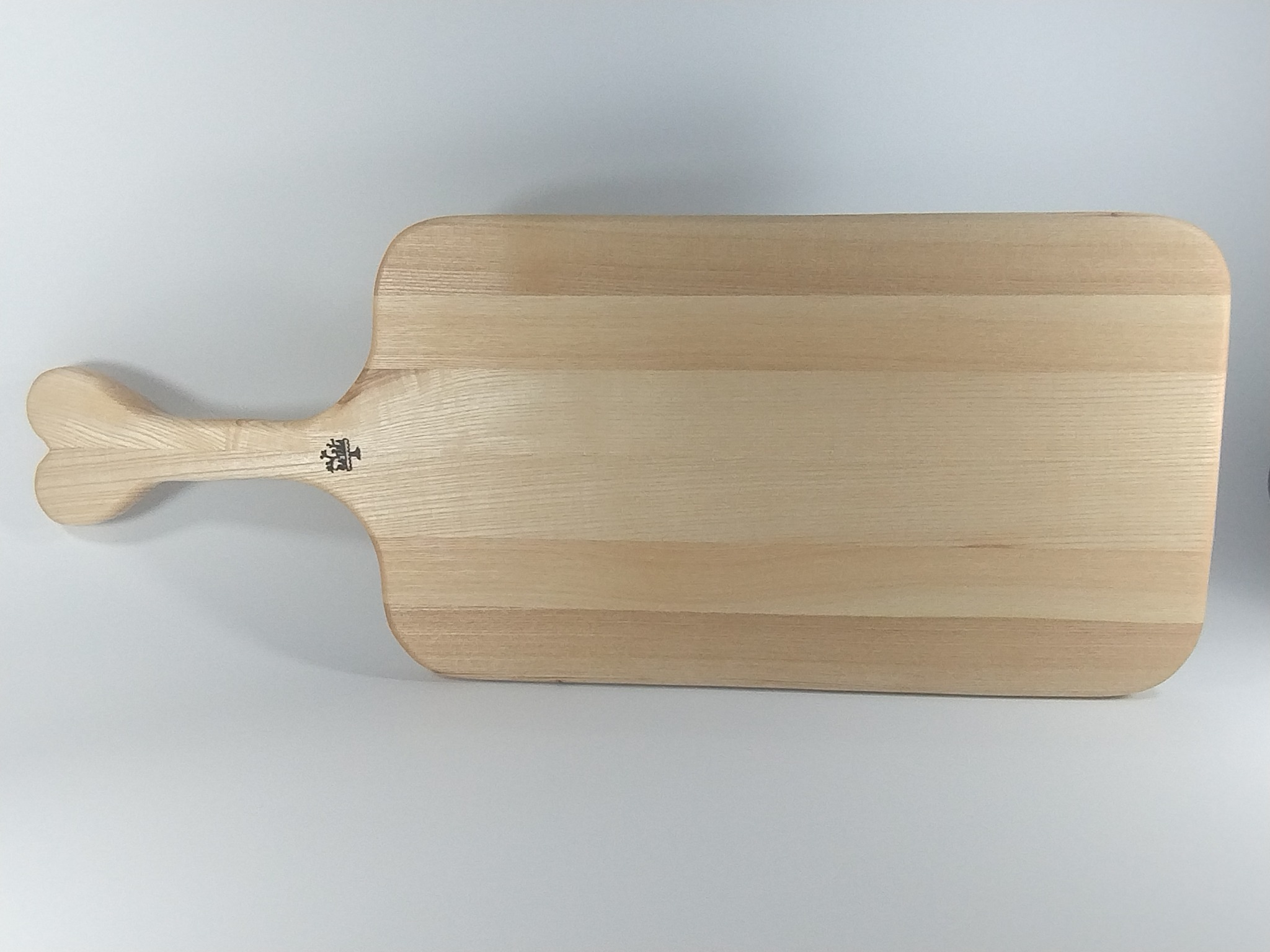Jasny, drewniany blat z uchwytem w kształcie serca, leżący poziomo na białym tle. Widoczne delikatne usłojenie drewna i małe logo na uchwycie.