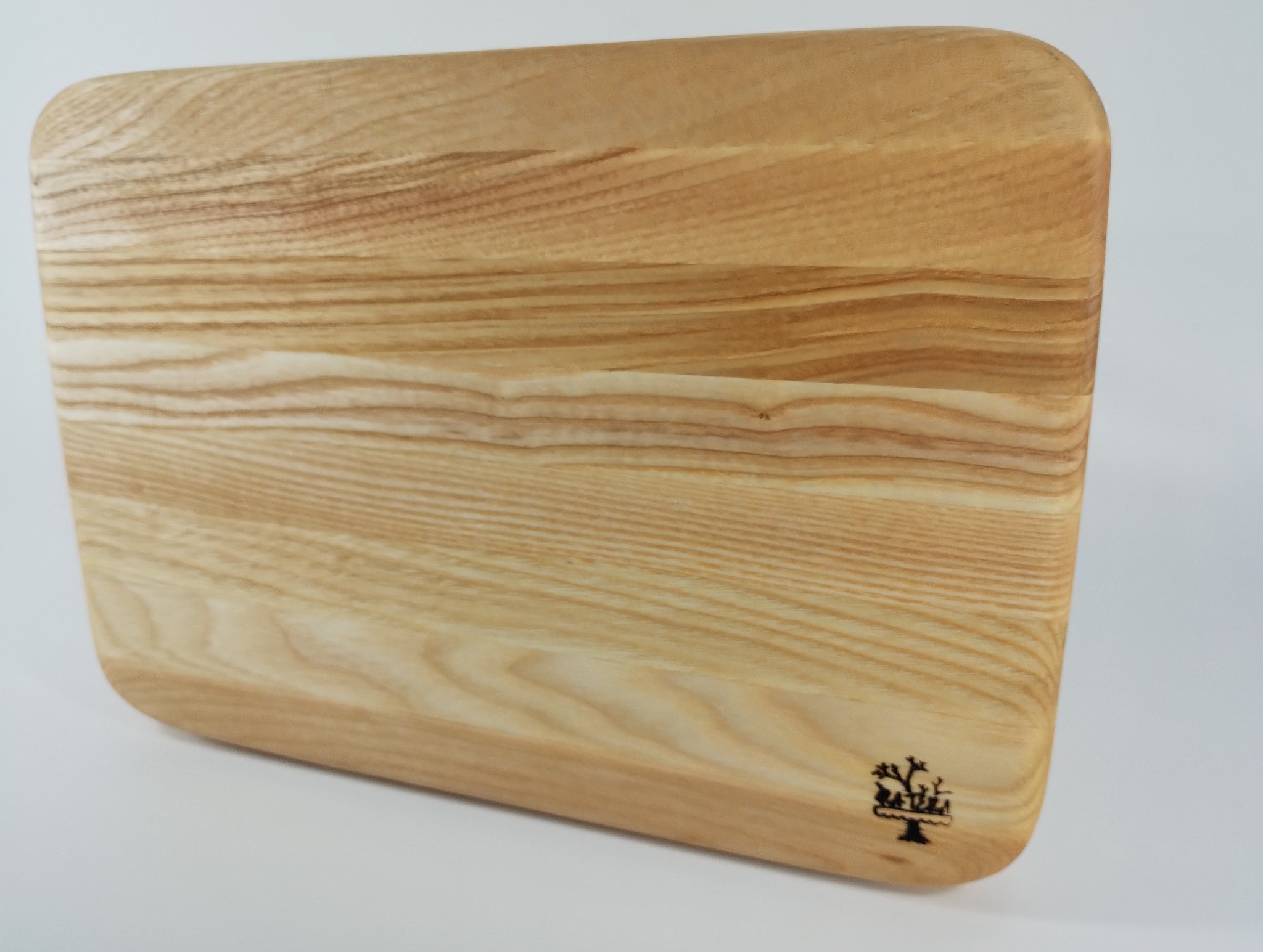 Drewniana deska do krojenia z jasnego drewna, z zaokrąglonymi rogami i delikatnym logo w prawym dolnym rogu, ukazująca naturalne usłojenie drewna.