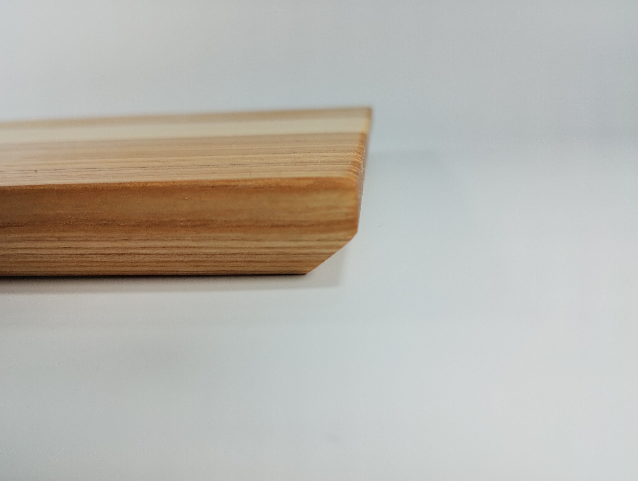Fragment blatu z jasnego drewna o widocznych słojach, z ukośnie ściętą krawędzią, na białym tle. Minimalistyczne ujęcie detalu wykończenia.