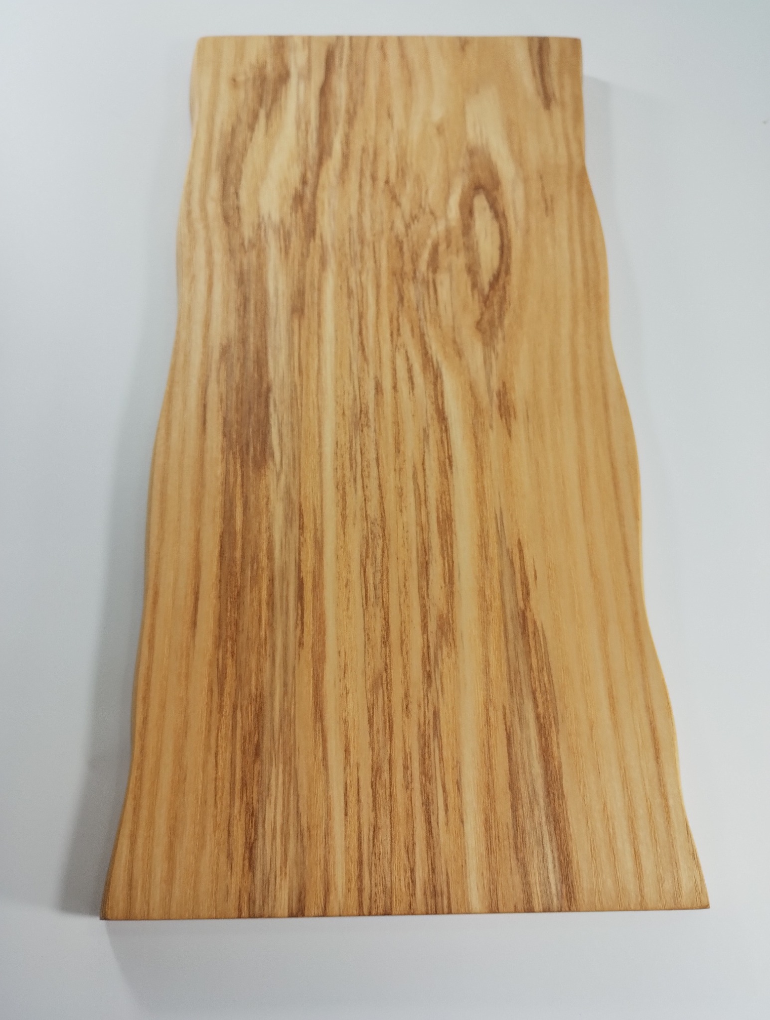 Drewniany blat o nieregularnym kształcie, z widocznym usłojeniem, leżący na białym tle. Naturalne wykończenie podkreśla unikalny charakter drewna.