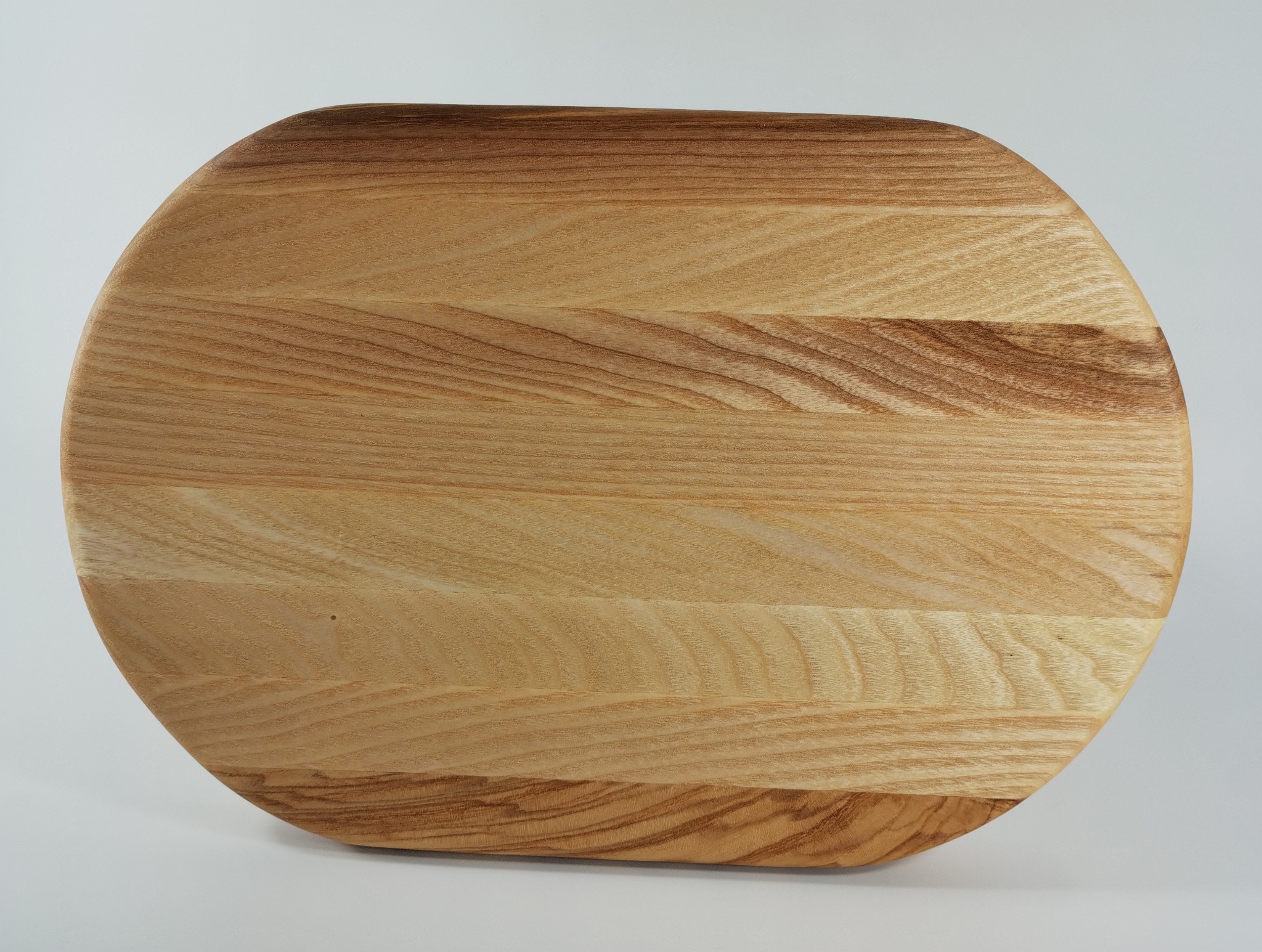 Owalna deska z jasnego drewna z wyraźnym usłojeniem, leżąca na białym tle. Widoczne naturalne przebarwienia i sęki w strukturze drewna. Gładka powierzchnia, zaokrąglone krawędzie.