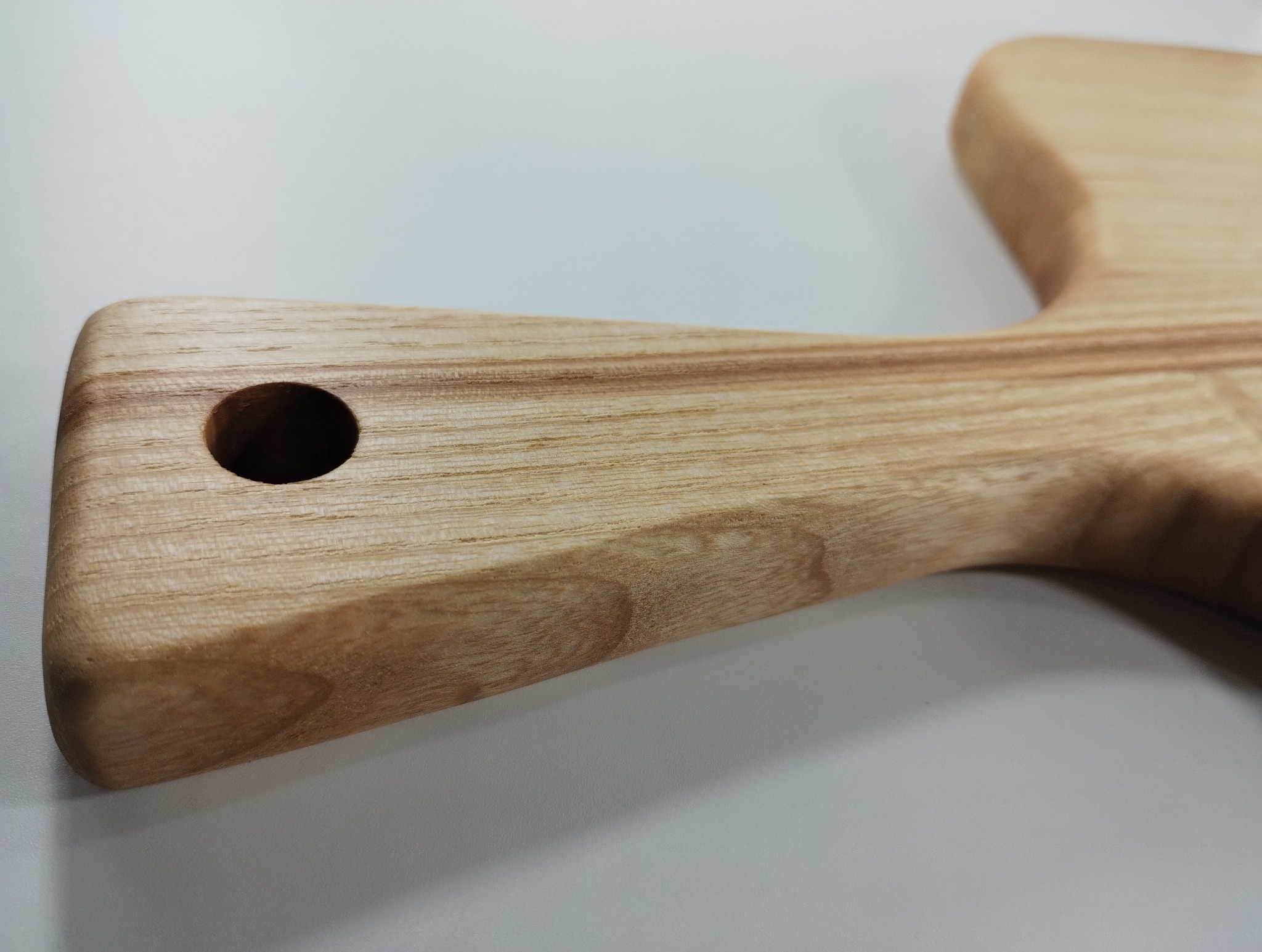 Jasna, drewniana deska do krojenia z uchwytem i otworem, leżąca na białym tle. Widoczne naturalne usłojenie drewna i gładkie wykończenie.