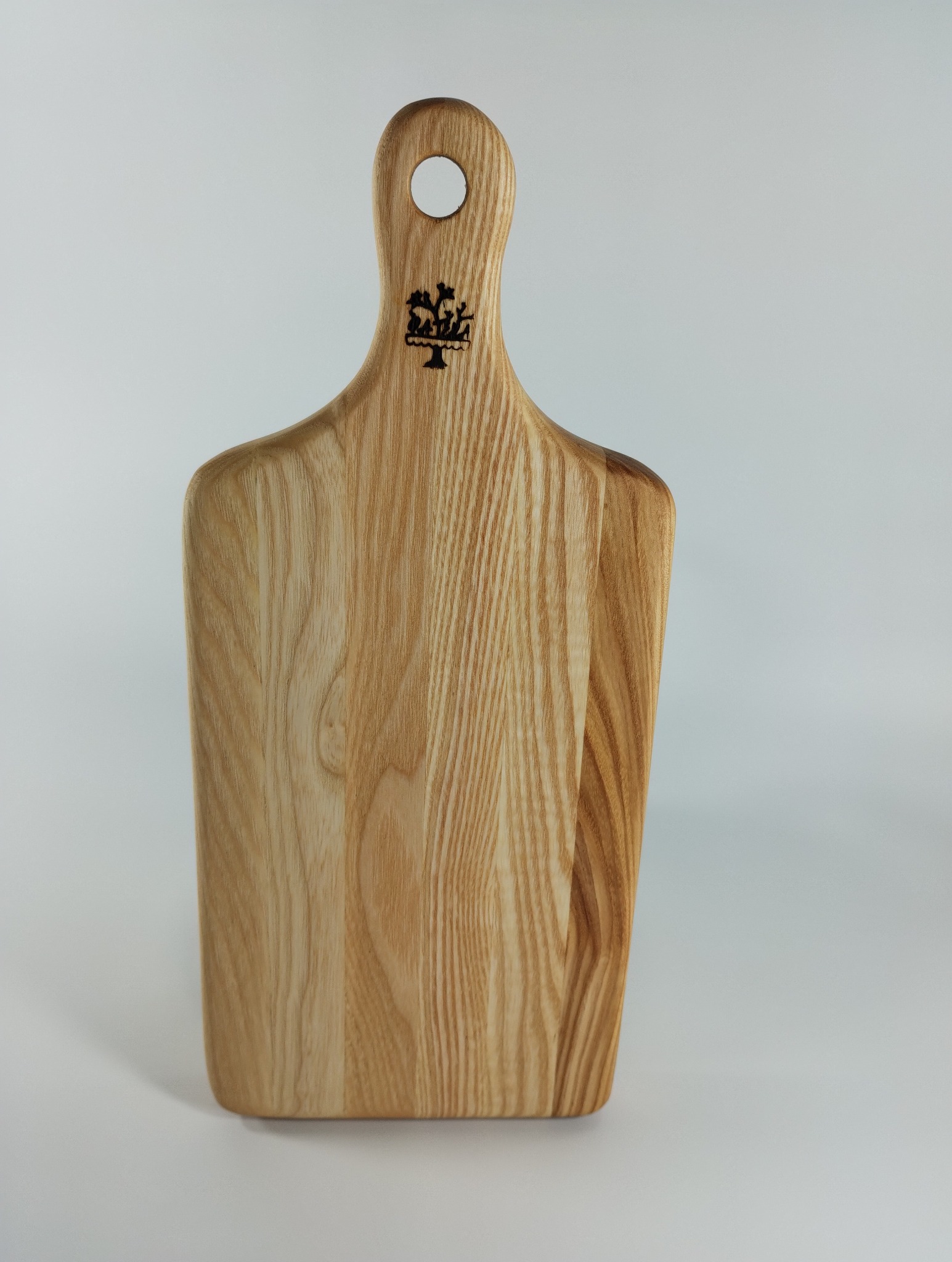 Drewniana deska do krojenia z uchwytem i wygrawerowanym logo, ukazująca naturalne usłojenie drewna na jasnym tle. Idealna do kuchni w stylu rustykalnym.