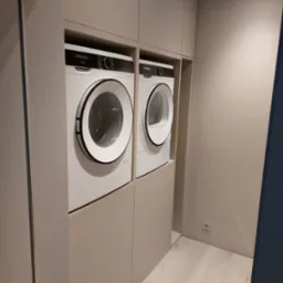 Białe pralki Siemens w zabudowie meblowej w odcieniach beżu. Minimalistyczny design, jasne panele podłogowe i gładkie fronty szafek.