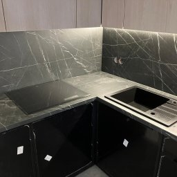 Custom-Made Furniture Meblowo - Meble na wymiar - Ciemna kuchnia z marmurowym blatem i płytą indukcyjną. Czarna zabudowa szafek, nowoczesny zlew. Oświetlenie LED pod szafkami górnymi. Minimalistyczny design.