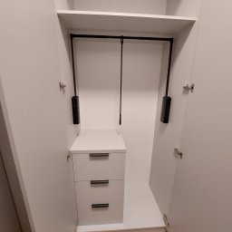 Wnętrze szafy wnękowej z trzema szufladami i drążkiem na ubrania z systemem opuszczania. Białe fronty, minimalistyczne uchwyty, otwarte drzwi.