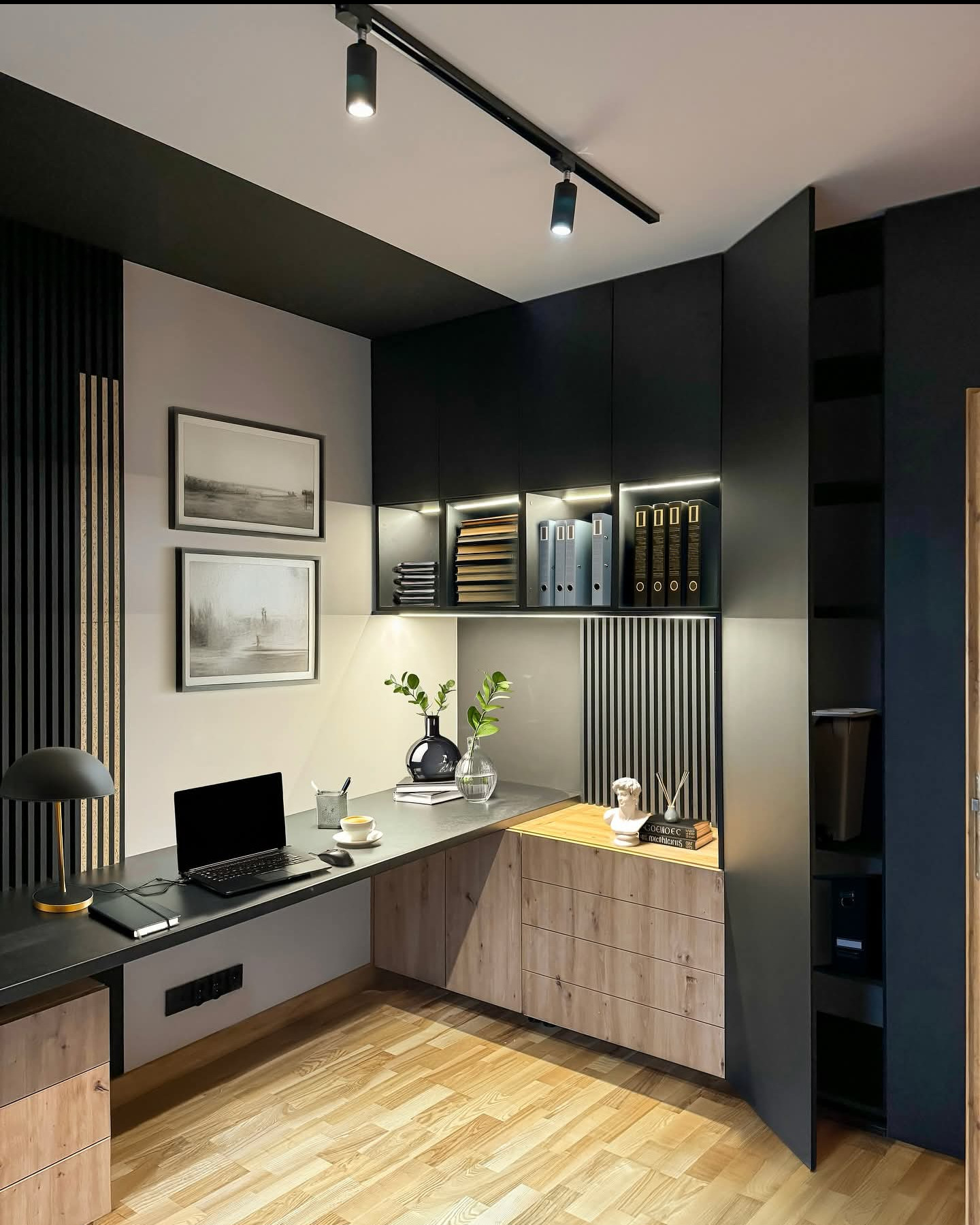 Nowoczesny gabinet z biurkiem, szafkami z drewnianymi frontami i czarnymi szafkami wiszącymi z oświetleniem LED. Na blacie laptop, lampka i dekoracje.