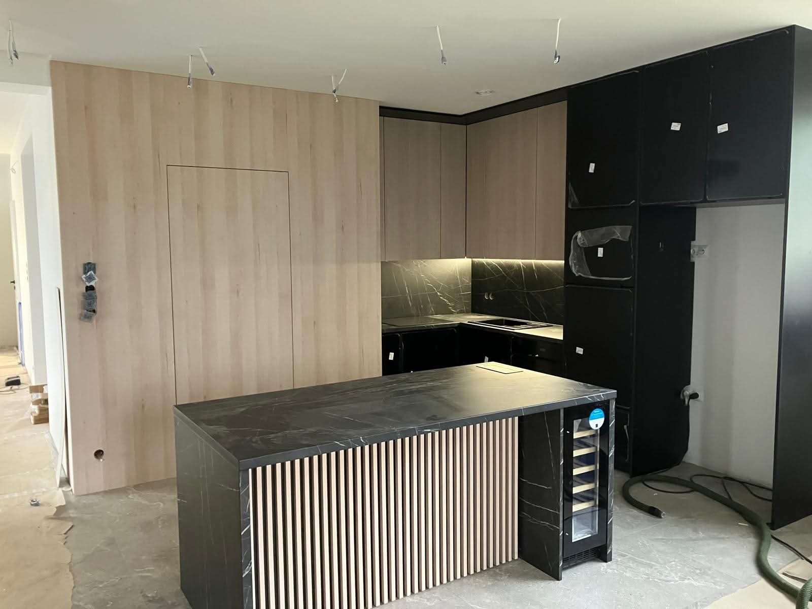 Nowoczesna kuchnia z wyspą i frontami w odcieniach beżu i czerni, marmurowy blat, Radlin. Widoczne niedokończone wykończenia.