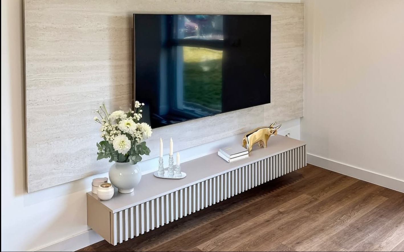 Nowoczesna szafka RTV w salonie z drewnianą podłogą i dekoracyjnym panelem ściennym. Na szafce wazon z kwiatami, świece i złota figurka byka.