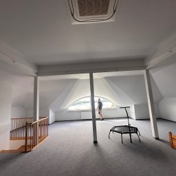 NJmalers - Jasne poddasze po remoncie: gładkie, białe ściany, szara podłoga, okno w kształcie łuku. Mężczyzna przy oknie. Widoczny fragment schodów z drewnianą barierką.