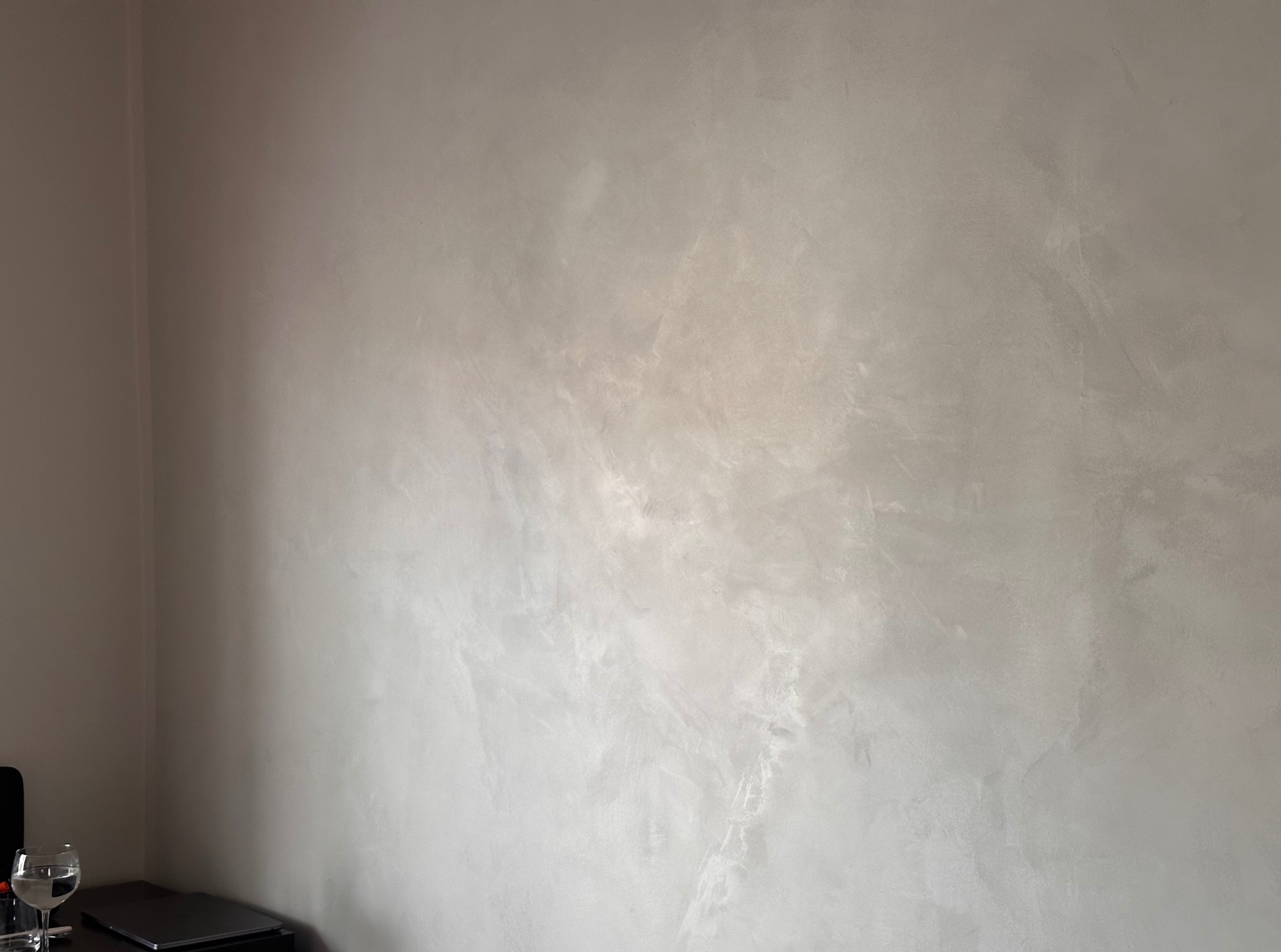 Ściana z efektem dekoracyjnym w odcieniach szarości i bieli, wykonana techniką imitującą marmur. Widoczny fragment blatu z laptopem i szklanką wody.