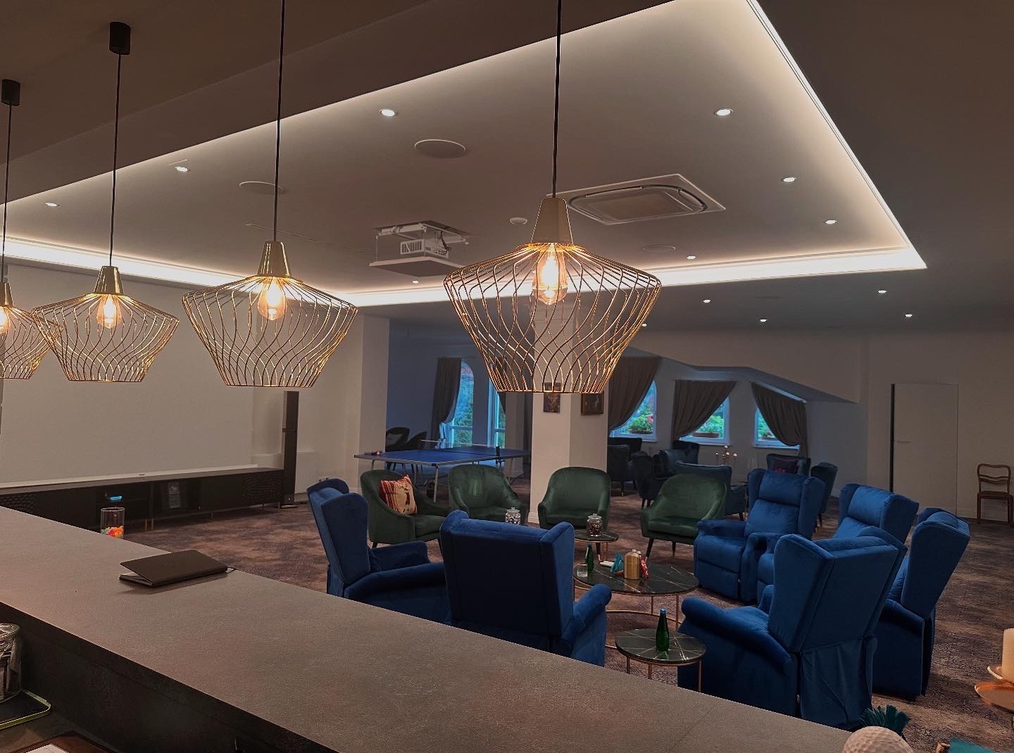 Ekskluzywne wnętrze z designerskimi lampami, komfortowymi fotelami i stołem do ping-ponga w tle. Oświetlenie LED podkreśla nowoczesny charakter pomieszczenia.