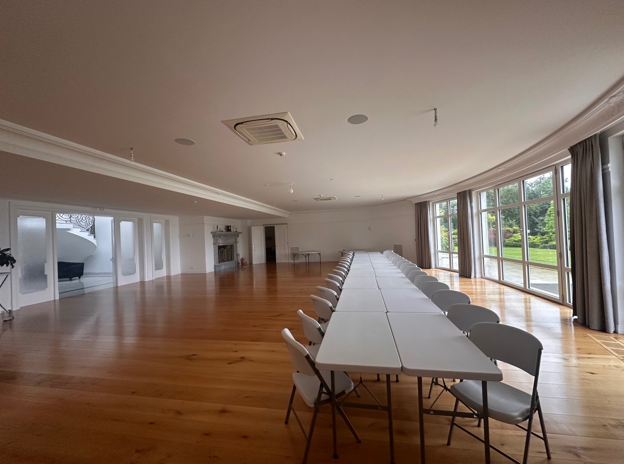 Jasne, przestronne wnętrze z parkietem i rzędem białych stołów i krzeseł. Duże okna z widokiem na zieleń. Świeżo pomalowane ściany i sufit.