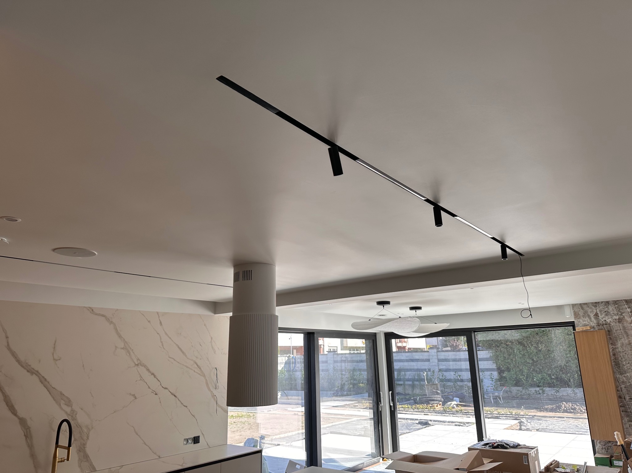 Nowoczesne oświetlenie szynowe w jasnym wnętrzu z marmurową ścianą i dużymi oknami. Minimalistyczny design lampy sufitowej.