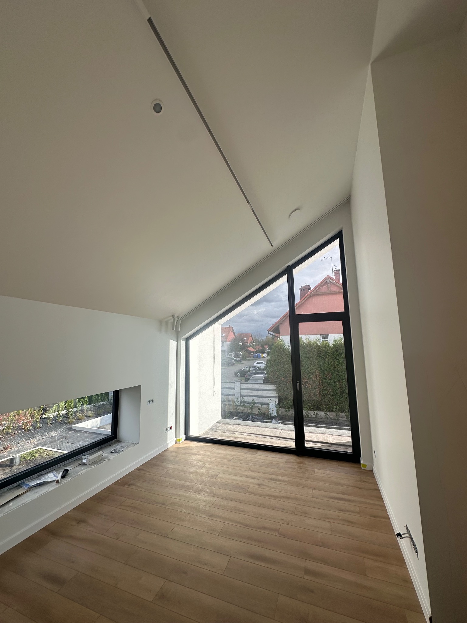 Jasne wnętrze po remoncie w Szczecinie: drewniana podłoga, białe ściany, okna z widokiem na zewnątrz. Minimalistyczny design i nowoczesne wykończenie.