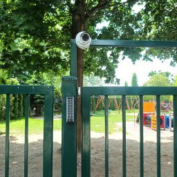 JAGO Grzegorz Brzoza - Zielona brama z domofonem i kamerą monitoringu na tle placu zabaw. Zabezpieczenie terenu, kontrola dostępu i nadzór wizyjny w przestrzeni publicznej.