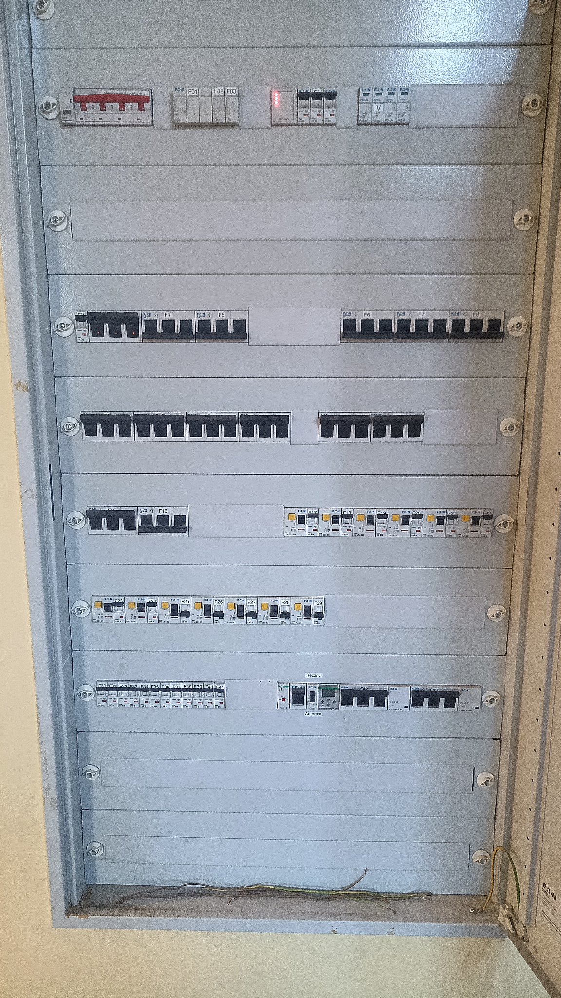 Rozdzielnica elektryczna z bezpiecznikami i wyłącznikami, widok z bliska. Szara obudowa, widoczne oznaczenia i przewody. Element instalacji elektrycznej.