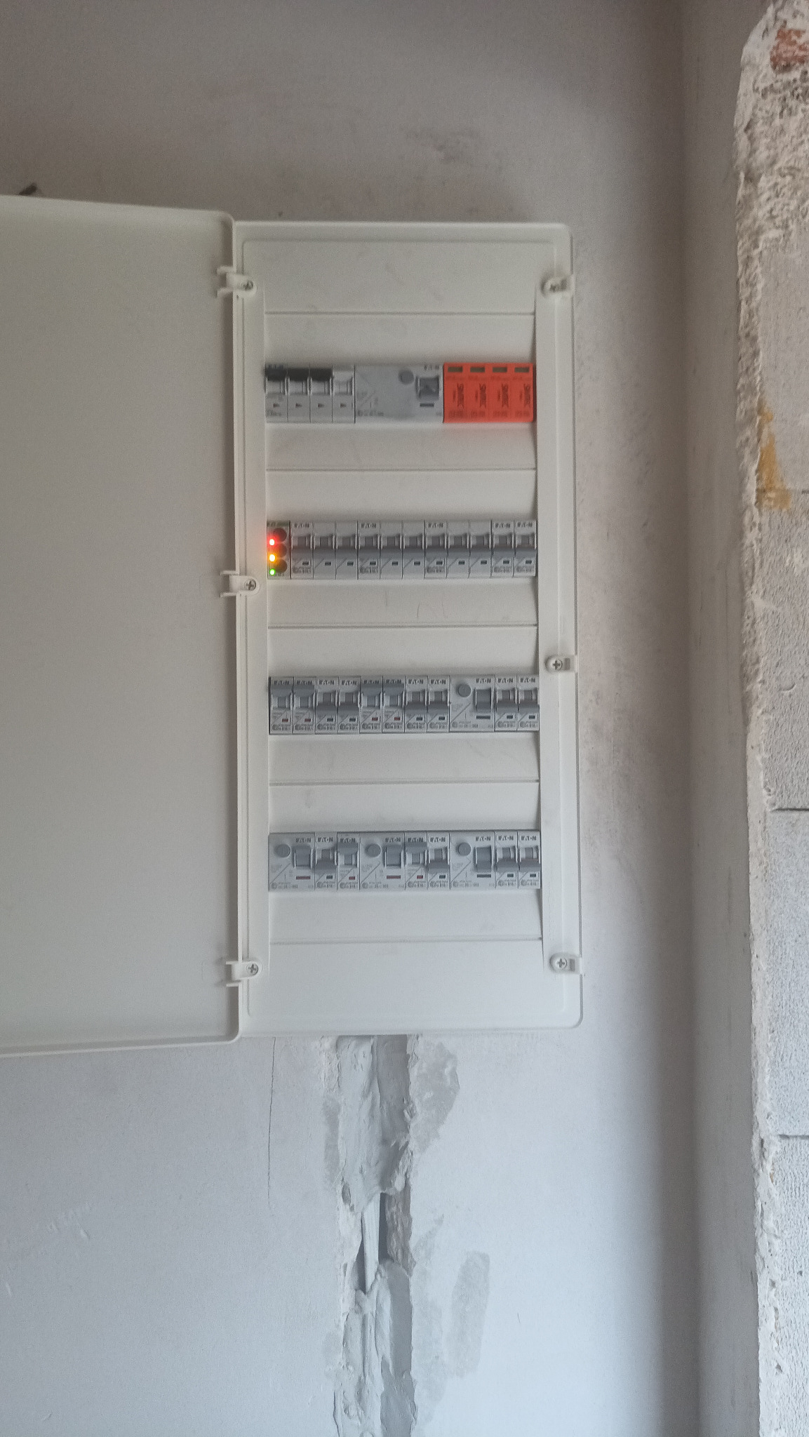 Otwarta skrzynka bezpiecznikowa z włączonymi bezpiecznikami, zamontowana na surowej ścianie we Wrocławiu. Widoczne kable i elementy instalacji elektrycznej.