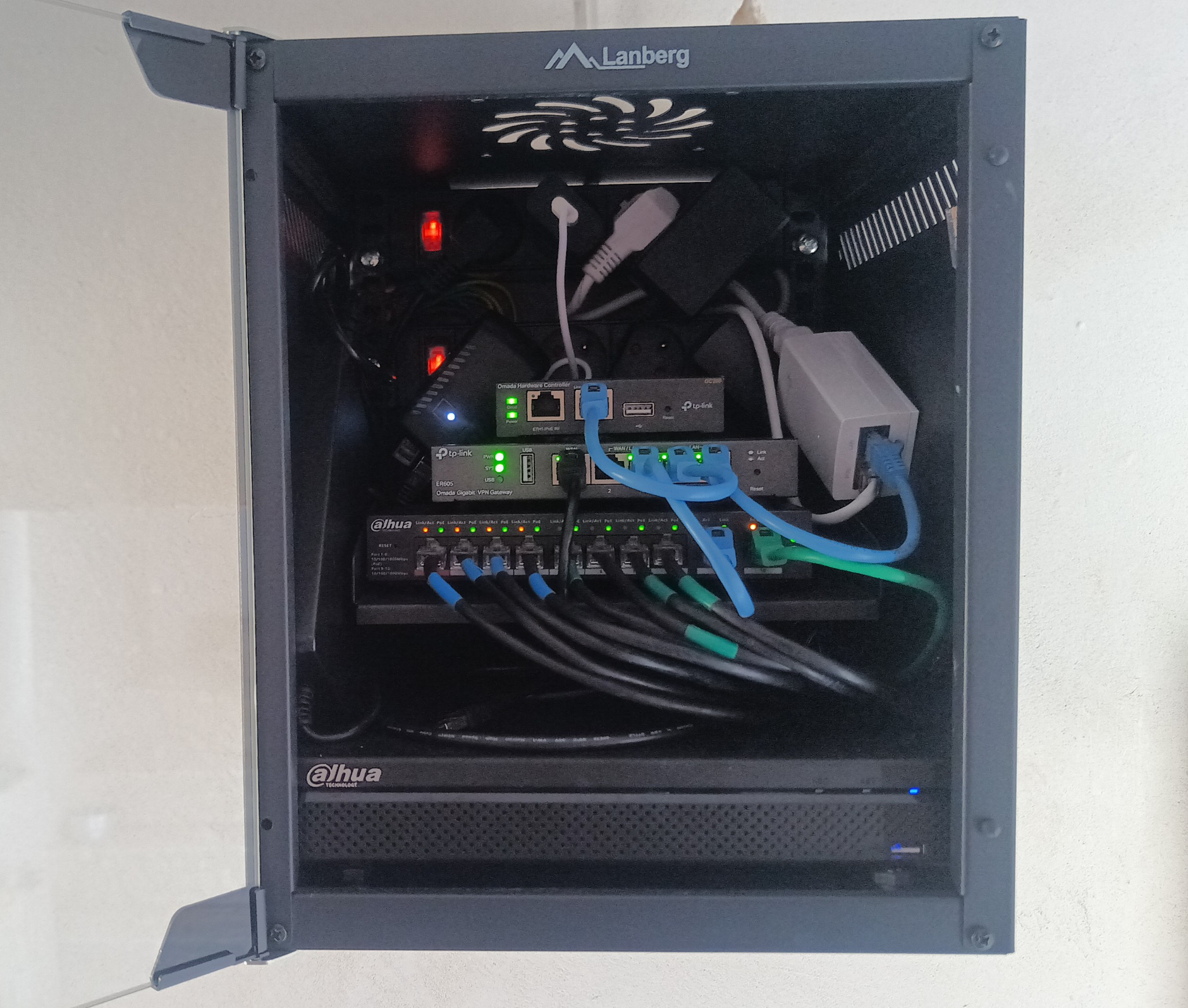 Zamknięta szafa rack Lanberg z zainstalowanymi urządzeniami sieciowymi Dahua i TP-Link, z widocznymi kablami ethernetowymi w kolorach niebieskim i zielonym.