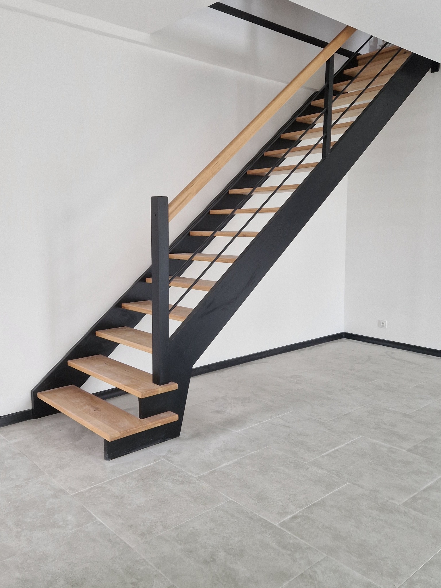 Nowoczesne schody z jasnego drewna i czarnej stali w minimalistycznym wnętrzu. Widok z dołu ukazuje konstrukcję i subtelne oświetlenie.