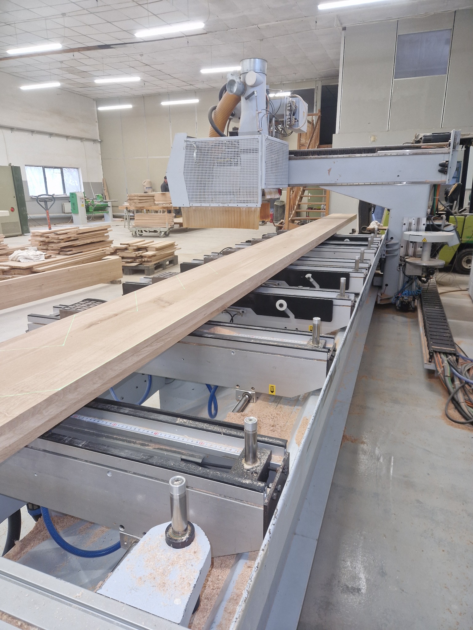 Obróbka deski na blat drewniany za pomocą frezarki CNC w warsztacie. Widoczne ślady obróbki i laserowe wyznaczenie wzoru.