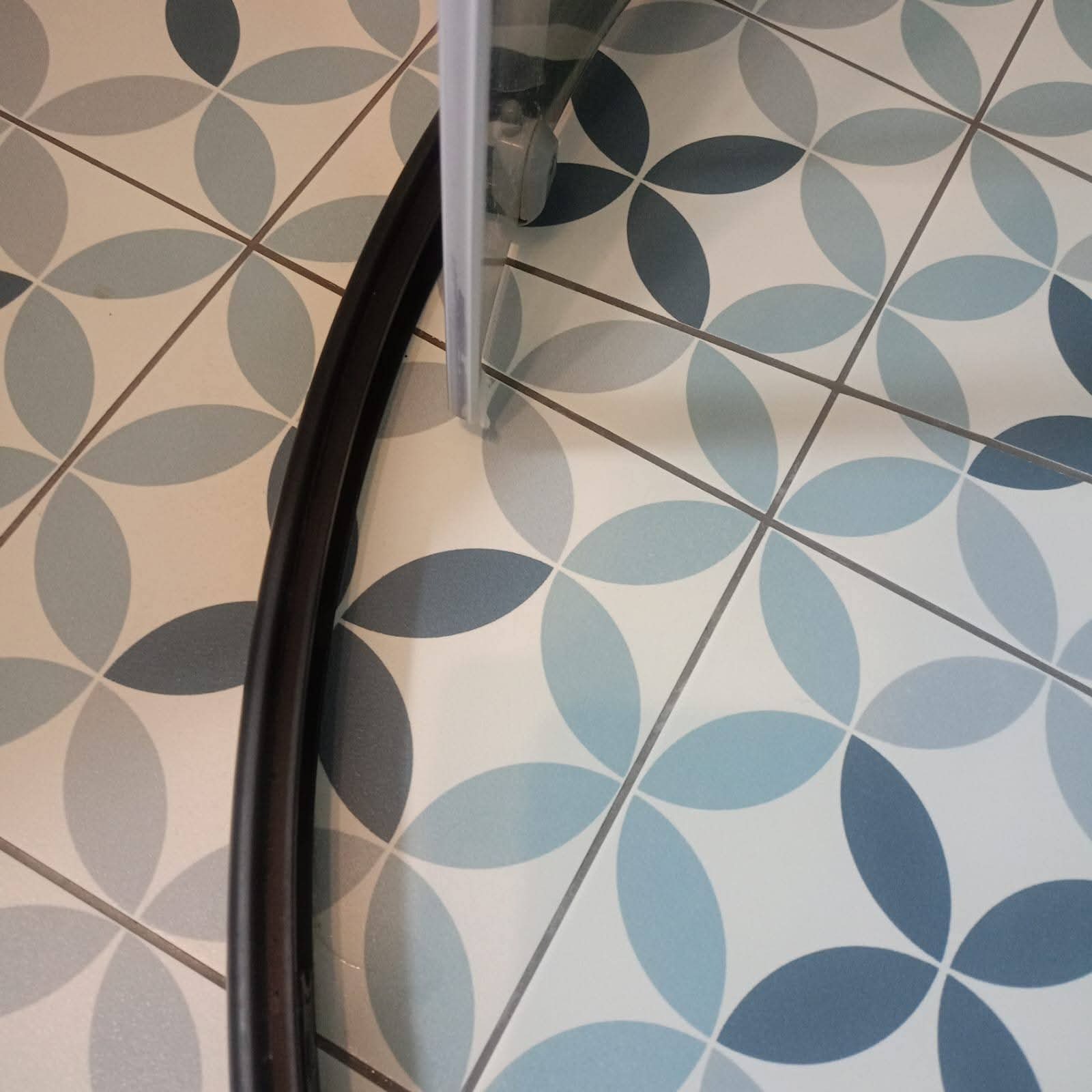 Wyczyszczona podłoga z wzorem kwiatowym w odcieniach błękitu i szarości, fragment kabiny prysznicowej z czarną uszczelką. Czystość i połysk płytek.