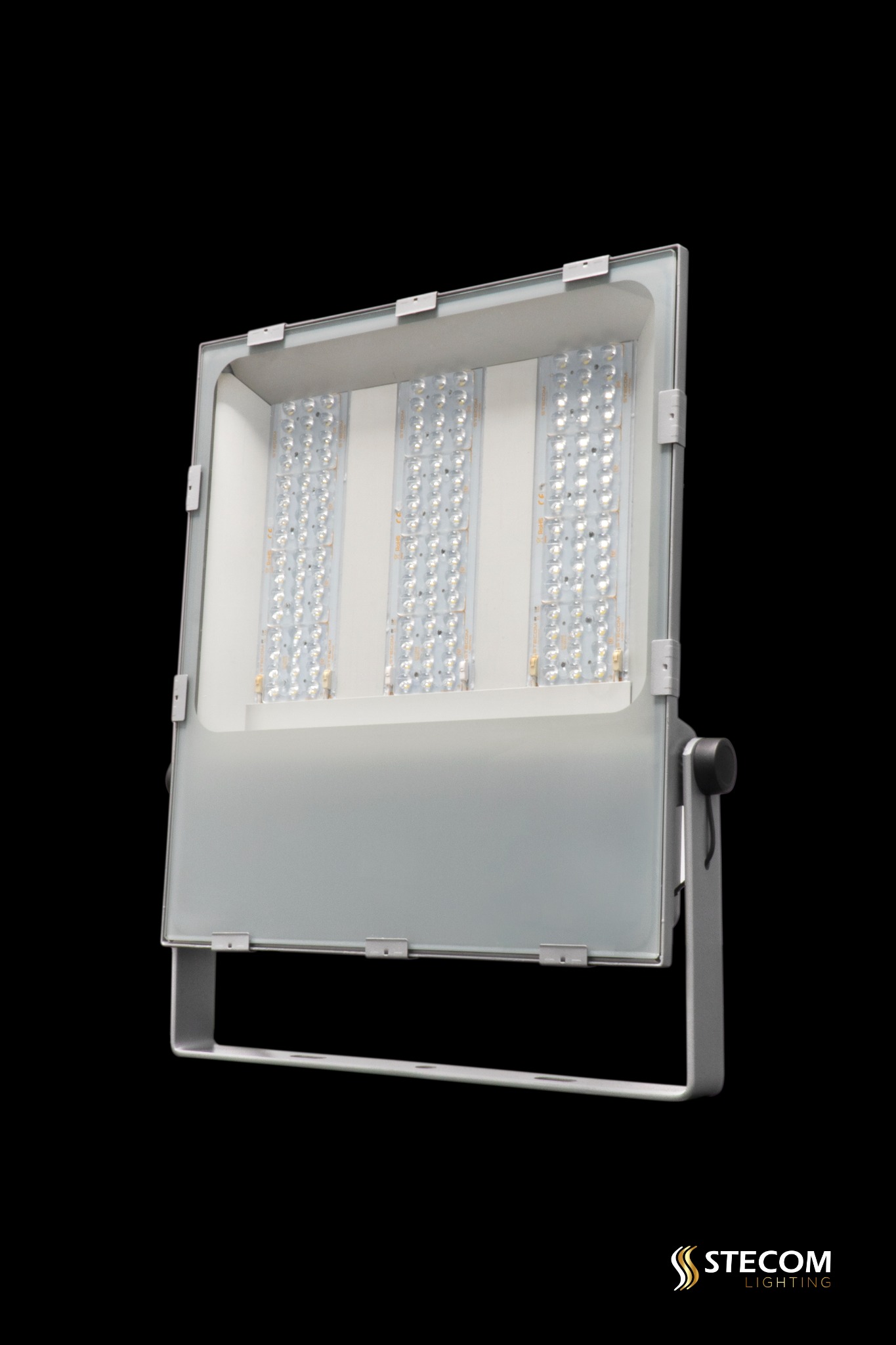 Lampa LED przemysłowa, reflektor z trzema panelami diodowymi, srebrna obudowa, widoczne mocowanie, na czarnym tle. Nowoczesne oświetlenie zewnętrzne.